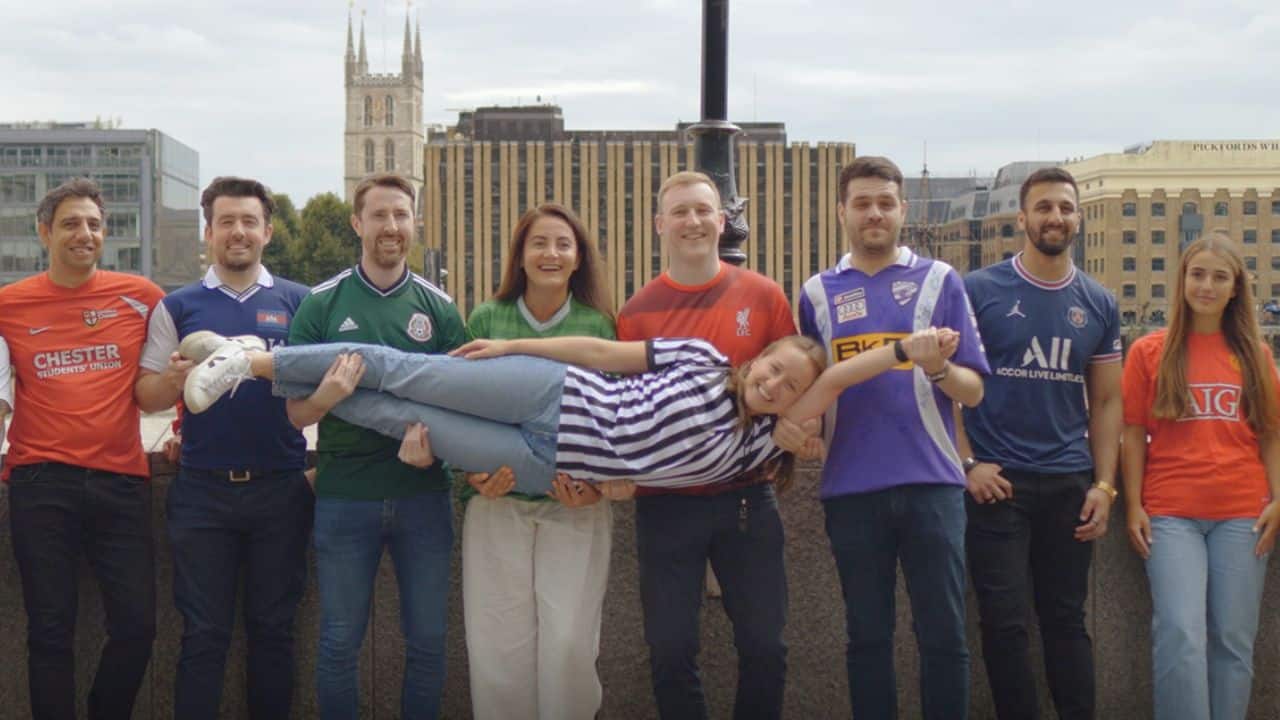 a team of men and women in football tops holding up the referee